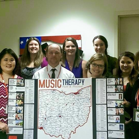 A group of music therapists posing with a presentation board about music therapy past and present in Ohio.