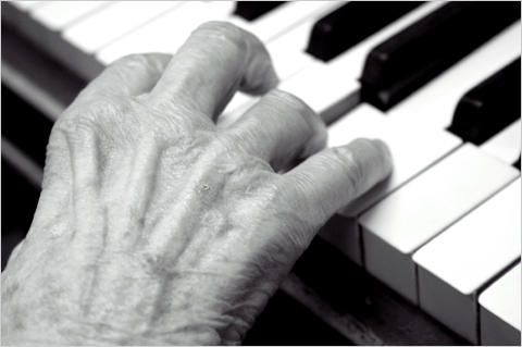 The hands of an older adult as they play the keys of a piano