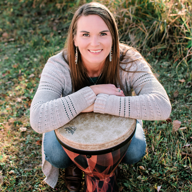 Brittany with a djembe drum, looking upward with a smile on her face.