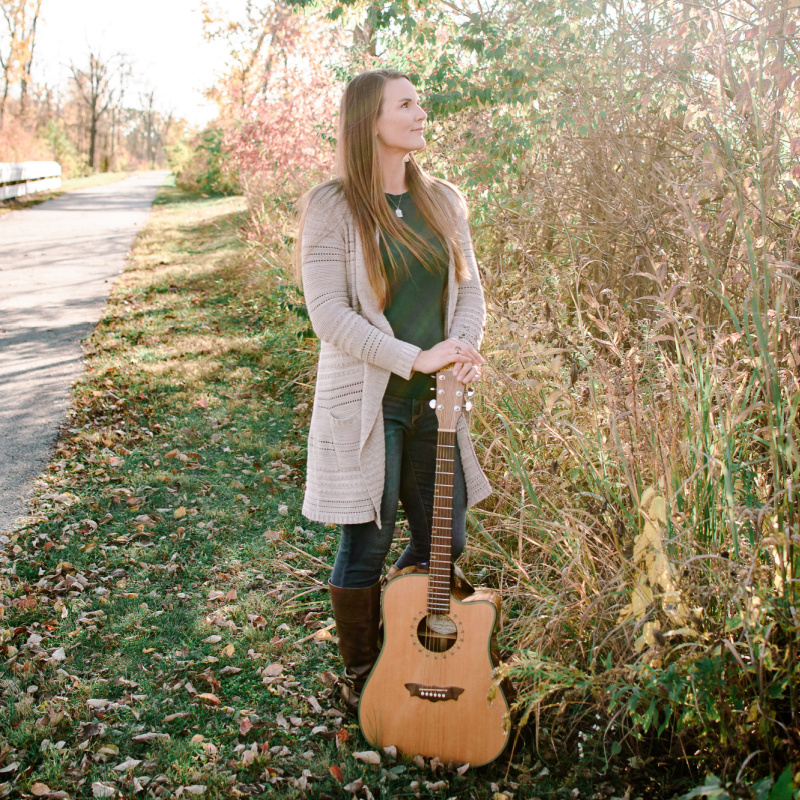 Brittany standing next to a path, holding a guitar. 